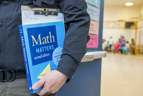 teacher holding a blue math matters text book in a classroom